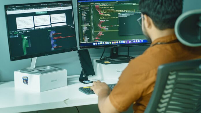AI Agent Operations 16 by 9 A person working at two computer monitors, representing AI agent operations and IT systems.